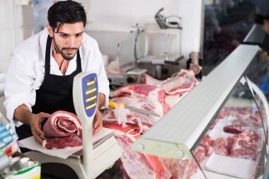 Adult man butcher is weighing meat for client in food shop